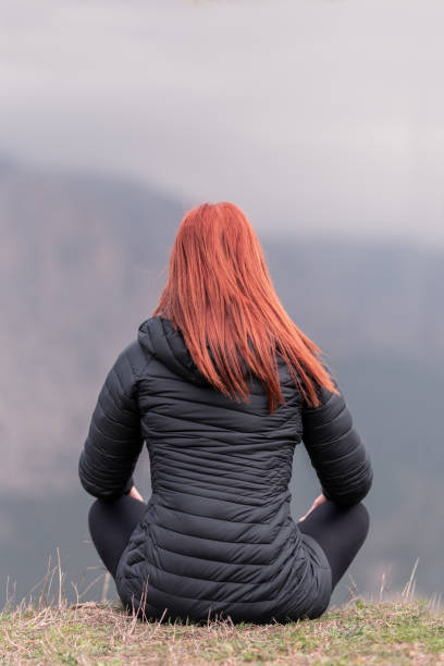 istock red-haired woman sitting on a cliff looking at the horizon 1380806890