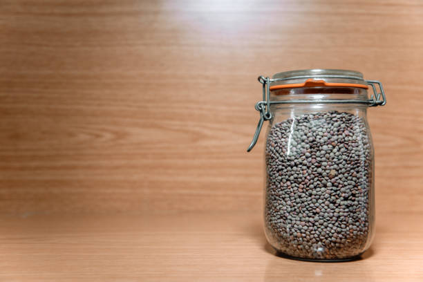 A glass jar full of lentils. Vegetal protein. Concept of storage of vegetables in the kitchen. Wood background. Copyspace.
