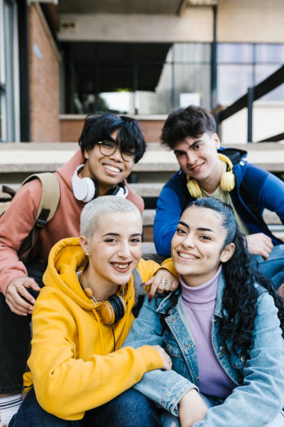 Vertical shot of multiracial young students sitting at school building entrance stock photo