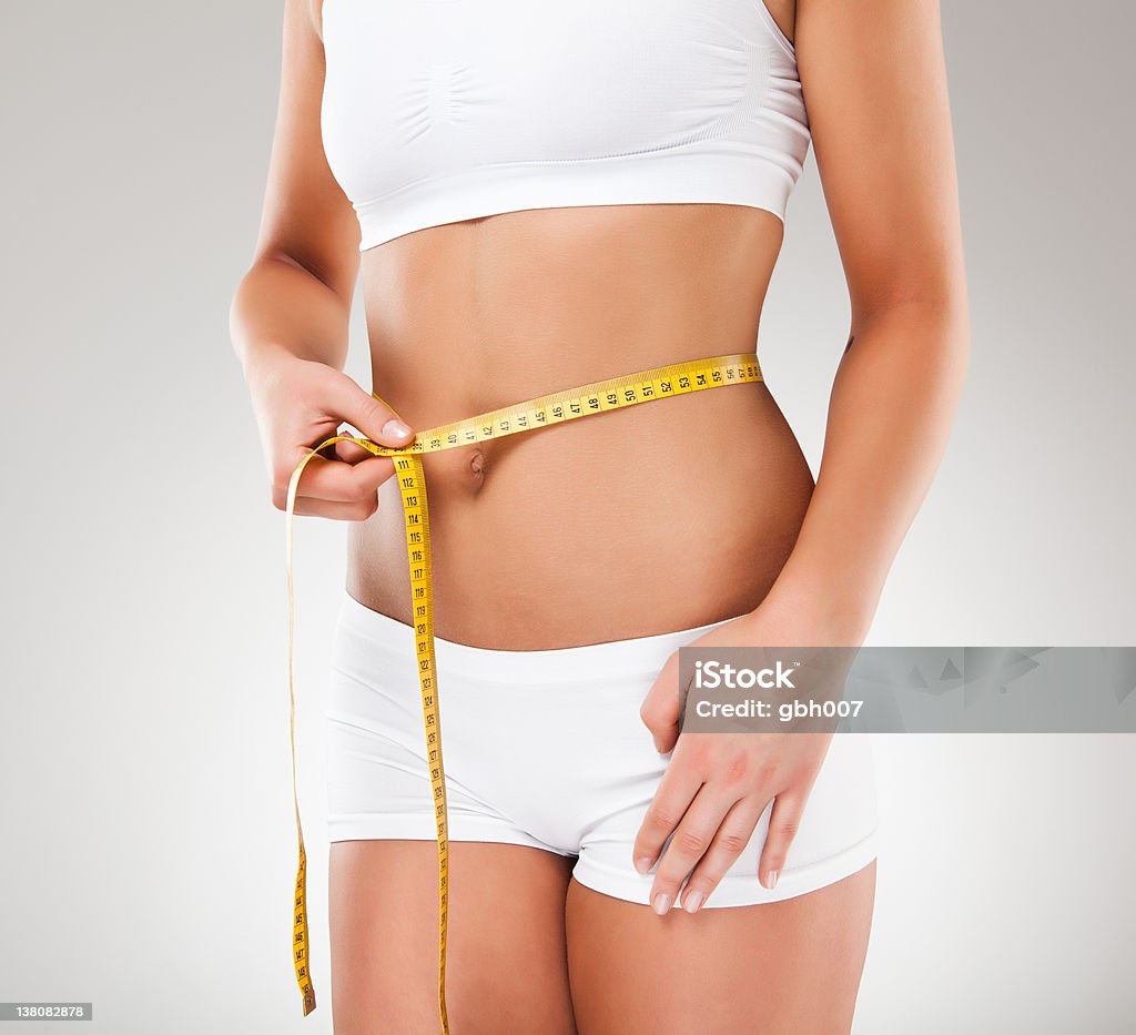 Slim woman measuring her body Slim woman measuring her body on gray background  20-24 Years Stock Photo