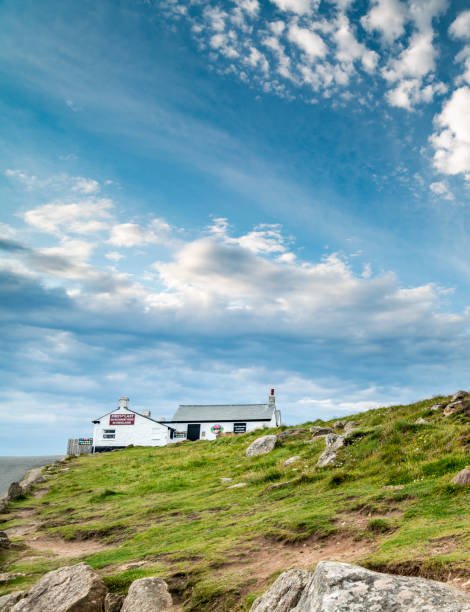 Perched on the westernmost tip of the southwest of England,the Atlantic Ocean below the ciffs,in the summer, near to sunset,a main tourist attraction,surounded by grassy slopes,covered in rocks.