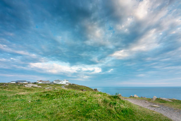 Young woman stands on rock headland above ocean, Cornwall