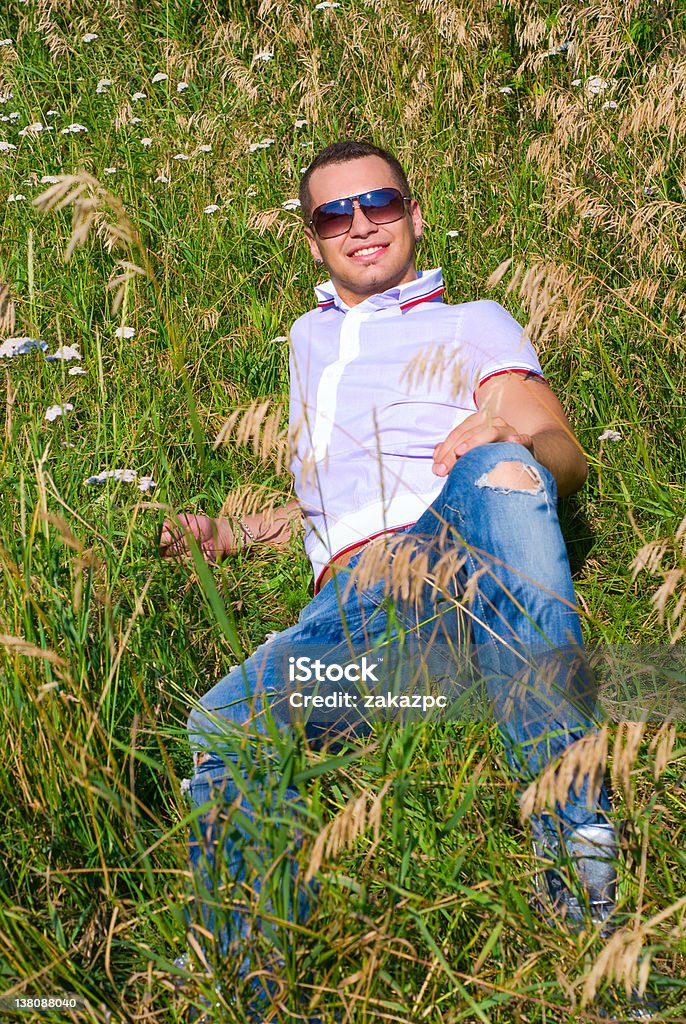 Happy young man in grass Young man in jeans with teeth smile is lying on summer field. Green grass surrounds him. 20-24 Years Stock Photo