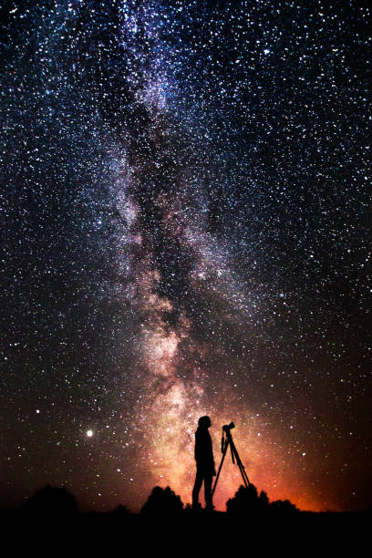 Silhouette of man on dark background. Photographer photographs landscape. Camera on tripod. Summer starry sky. Stars on sky. Beautiful night landscape. Long exposure. Milky way. Abstract. Deep space stock photo
