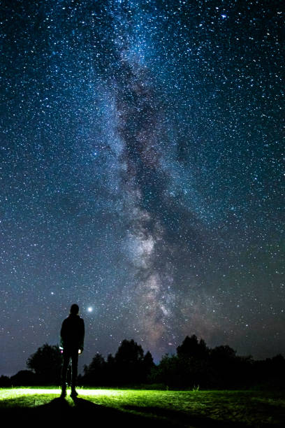 istock Silhouette of man on dark background. Light beam from flashlight. Summer starry sky. Stars on sky. Beautiful night landscape. Long exposure. Milky way. Abstract. Deep space 1380899011