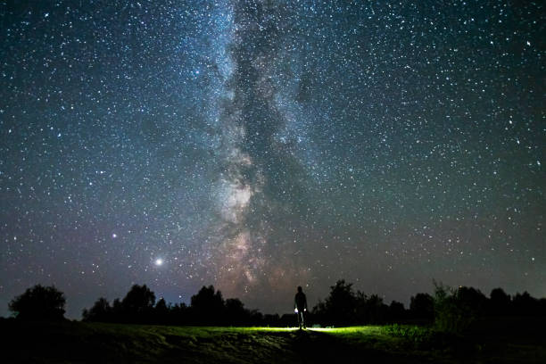 istock Silhouette of man on dark background. Light beam from flashlight. Summer starry sky. Stars on sky. Beautiful night landscape. Long exposure. Milky way. Abstract. Deep space 1380899539