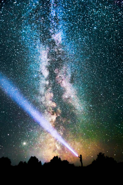 istock Silhouette of man on dark background. Light beam from flashlight. Summer starry sky. Stars on sky. Beautiful night landscape. Long exposure. Milky way. Abstract. Deep space 1380903276