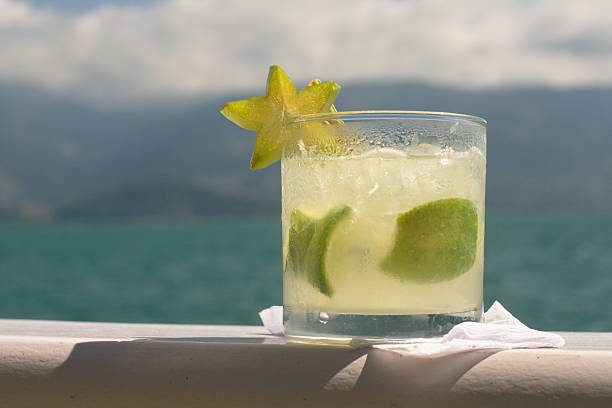 Caipirinha with Star Fruit Caipirinha (cocktail) with star fruit garnish, with beautiful blue-green water and hills in the background. starfruit stock pictures, royalty-free photos & images