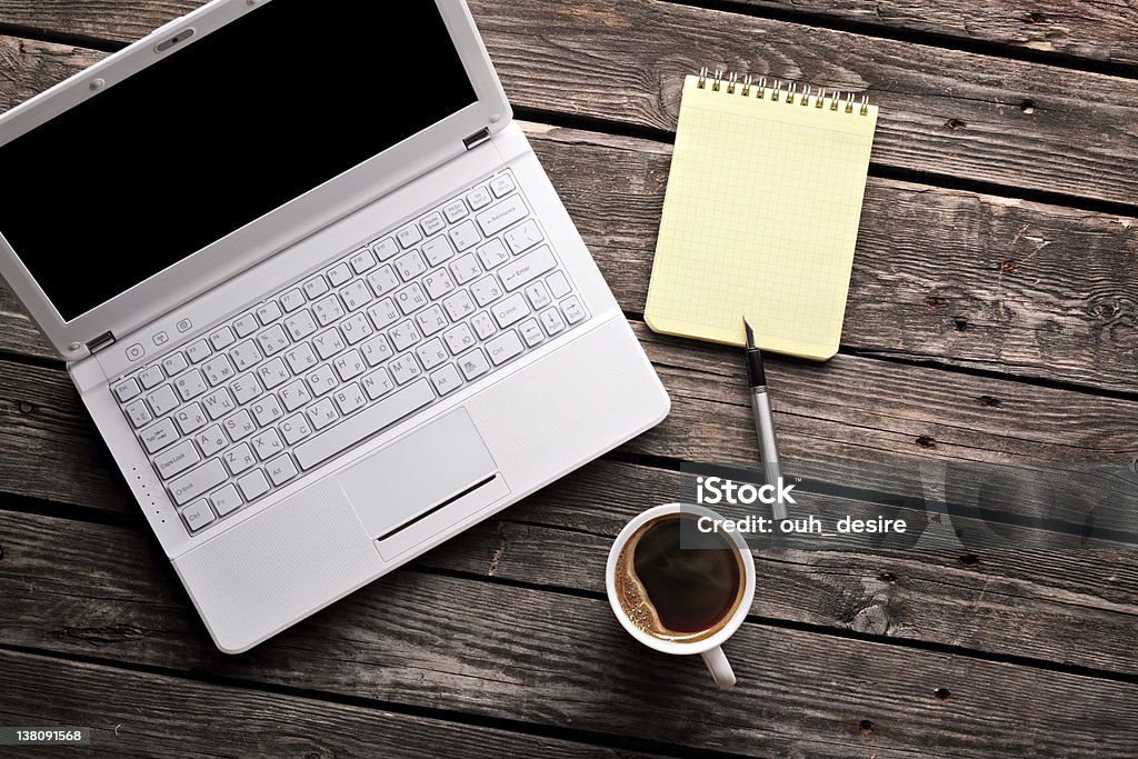 Mug of coffee and a laptop lie on wooden boards Laptop (notebook) with cup of coffee and notepad with pen on old wooden table. Laptop Stock Photo