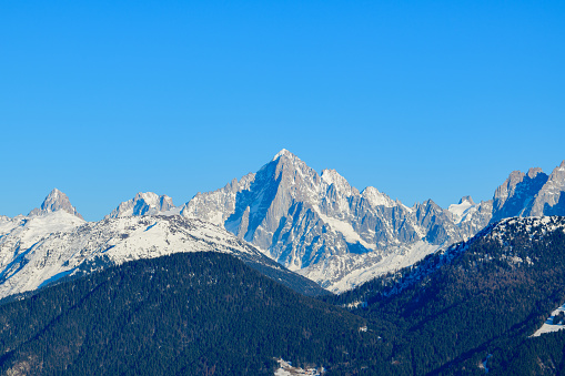 This landscape photo was taken in Europe, in France, Rhone Alpes, Savoie, in the Alps, in winter. We see the Green Needle surrounded by snowy forests, under the Sun.