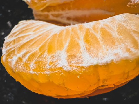 A macro image of a peeled clementine with a black background.