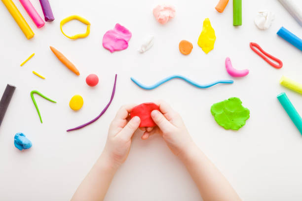 istock Baby hands holding and kneading red modeling clay on white table background. Closeup. Point of view shot. Toddler development. Making different colorful shapes. Top down view. 1380977824