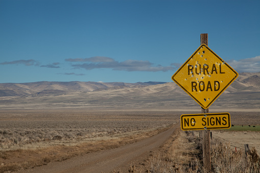 Yellow rural road sign with bullet holes in a remote area.