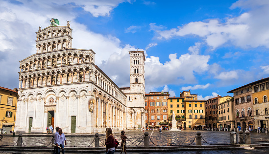 People strolling in Piazza San Michele in Lucca, where overlooks the majestic Basilica Church of San Michele in Foro, whose construction dates back to the 8th century (3 shots stitched)