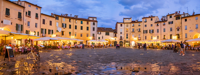Tourists visiting the Piazza dell'Anfiteatro of Lucca, an elliptical shape square surrounded by a ring of buildings that follows the former second century Roman amphitheater of the city (2 shots stitched)