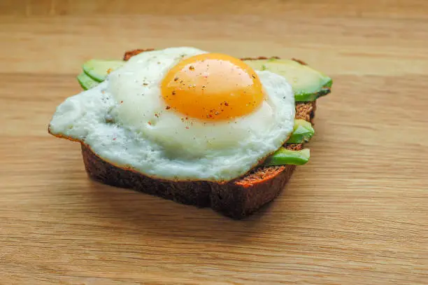 sandwich black Borodino bread with avocado and fried egg pepper salt on a wooden board