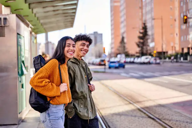 Photo of teenage couple waiting at the train or tram stop. young students with a guitar and a ukulele in its case.