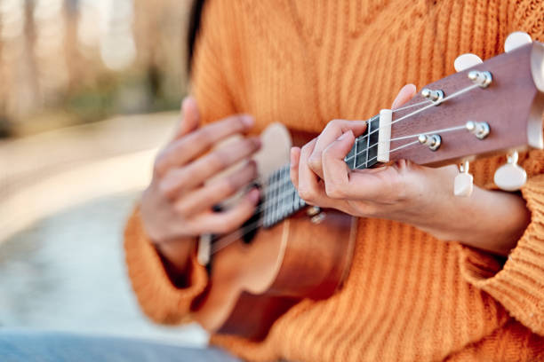 primo piano della ragazza che suona l'ukulele in un giardino con chitarra acustica, messa a fuoco selettiva delle mani della donna che suonano le corde dell'ukulele. - uke foto e immagini stock