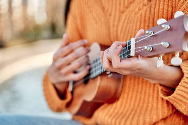 Close-up of girl playing ukulele in a garden with acoustic guitar, selective focus of woman hands playing ukulele strings. Close-up of girl playing ukulele in a garden with acoustic guitar, selective focus of woman hands playing ukulele strings. ukulele stock pictures, royalty-free photos & images