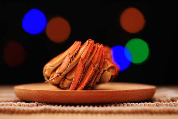 Yokohama, Kanagawa, Japan - February 15, 2025: A close-up shot of a person's hands using scissors to cut snow crab legs at an all-you-can-eat crab course in Yokohama Chinatown. The bright orange crab legs are served on a white plate. The focus is on the action of cutting the crab, with the person's patterned sleeves visible. The warm lighting suggests a dining atmosphere.