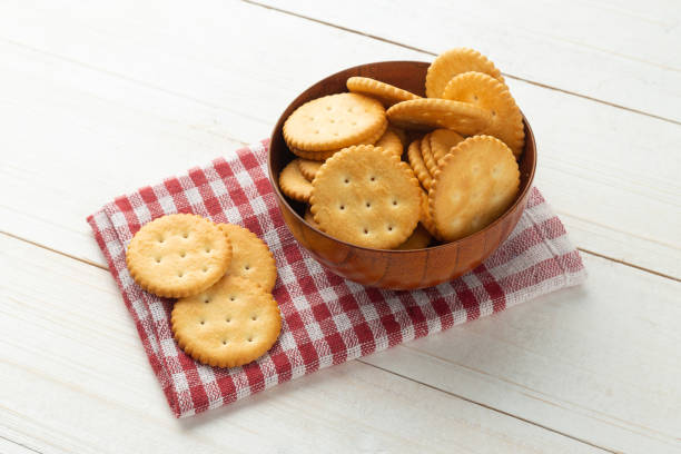 galletas de galletas redondeadas en un tazón de madera con mantel sobre fondo de mesa de madera blanca - yellow cheese thin portion fotografías e imágenes de stock