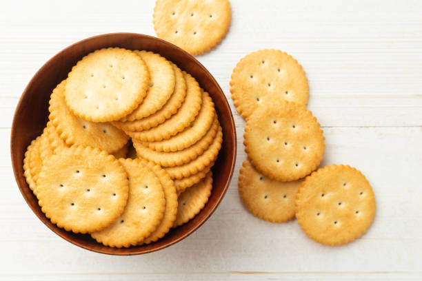 zaokrąglone ciasteczka krakersowe w drewnianej misce na białym drewnianym tle stołu - yellow cheese thin portion zdjęcia i obrazy z banku zdjęć