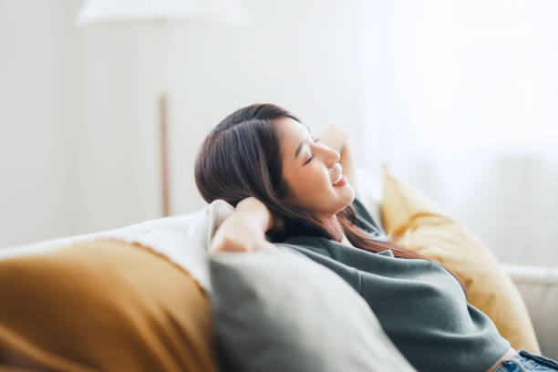 Relaxed young asian woman enjoying rest on comfortable sofa at home, calm attractive girl relaxing and breathing fresh air in home stock photo