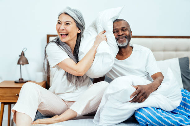 imagen cinematográfica de una feliz pareja multiétnica de mayores. - bed couple pillow fight men fotografías e imágenes de stock