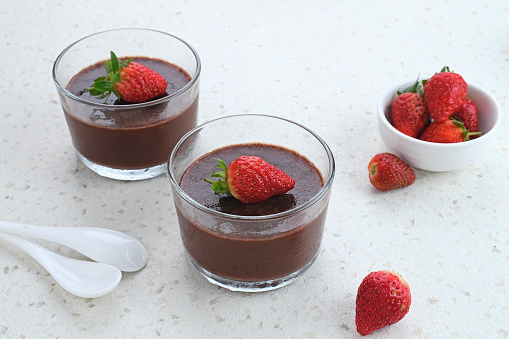 Chocolate pudding with strawberries in glass on white table. Selected focus.
