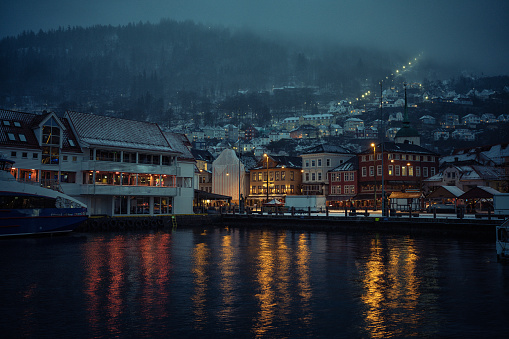 Snow storm over the city during a winter day, while city life proceeds as normal. View to Bryggen district, cars, pedestrians and dark evening blue light