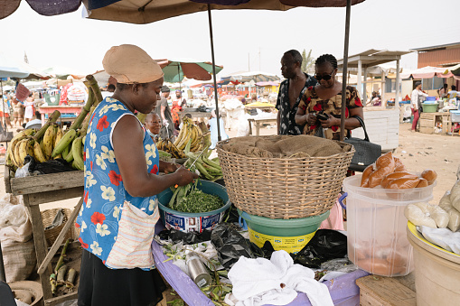 Accra, Ghana - 5 Februar 2022:  african market woman sells vegetables under a sunshade at a market in Accra