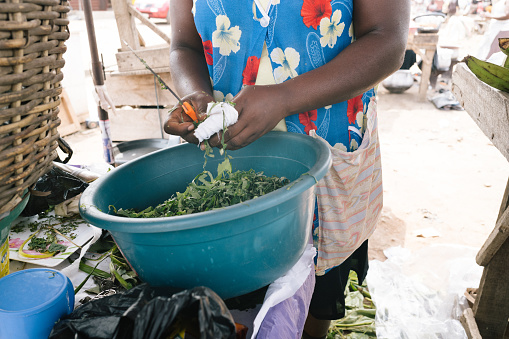 Accra, Ghana - 5 Februar 2022: african market woman  cuts the fresh spinach into small pieces for the customers