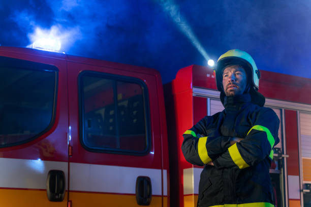 istock Low angle view of firefighter with fire truck in background at night. 1381109370