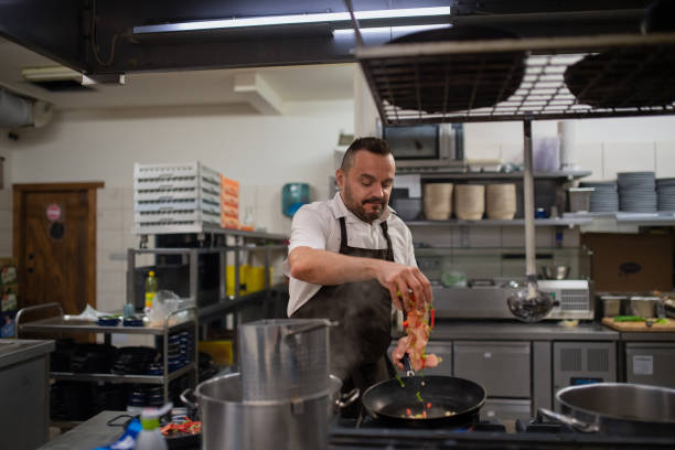 istock Mature chef adding chopped vehetagles to pan indoors in restaurant kitchen. 1381119538