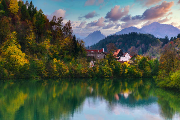 Amazing autumn landscape of a village in the Alps. View of the reflection of the fall colorful forest in the water of the river and of the mountain range in the distance at sunset. stock photo
