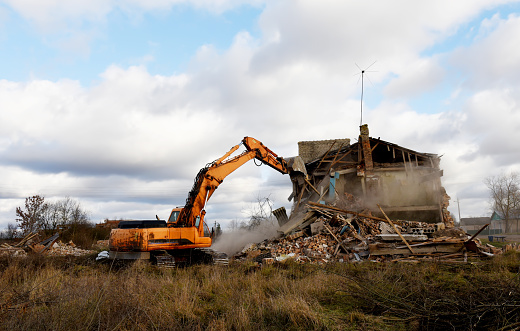 Excavator during demolition the house in the rural. Renovation old home and construction project. Backhoe demolishes building. Tearing Down a Houses. Destroy concrete for recycling and reuse.