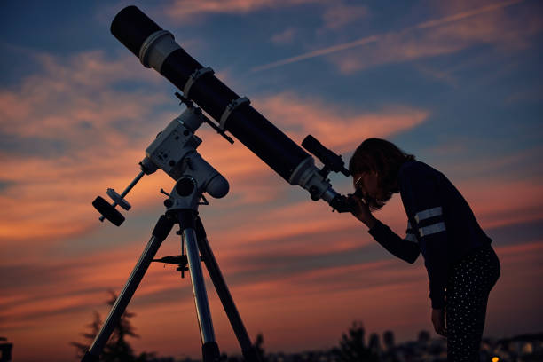 istock Girl with astronomical telescope stargazing under twilight sky. 1381160410