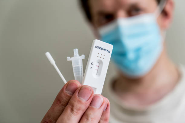 istock Man wearing face mask holding Covid-19 rapid antigen test kit and cassette with positive result of rapid diagnostic test. 1381177458