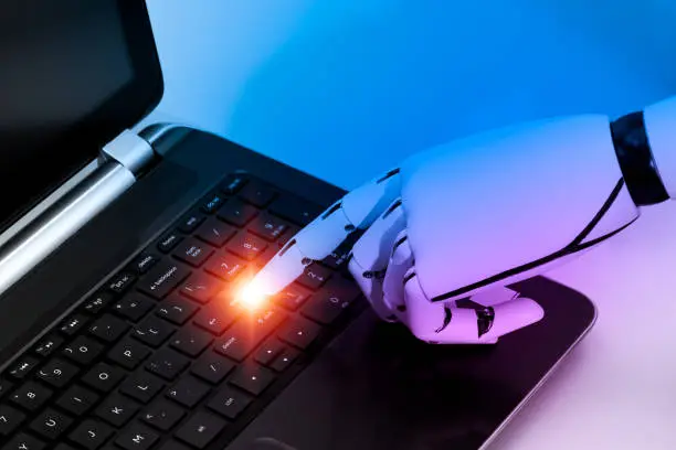 Photo of The robot's hand indicates that the enter key on the labtop computer's keyboard should be pressed. The concept is based on the internet of things and artificial intelligence robotics.