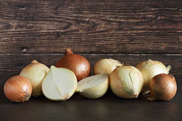 istock Fresh half and whole onions on dark wooden background. 1381218549