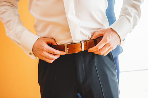 Groom in blue pants and a white shirt fastens his leather belt. grooms mourning. Wedding details