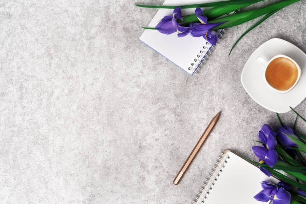 istock Spring women's workspace top view with beautiful iris flowers, notepad, pen and coffee on grey stone background. Flat lay with copy space. 1381228474