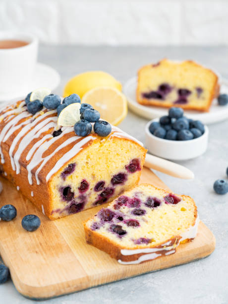istock Lemon blueberry cake with lemon icing and fresh berries on top on the board on a gray concrete background with cup of tea. Selective focus. Copy space. 1381235855
