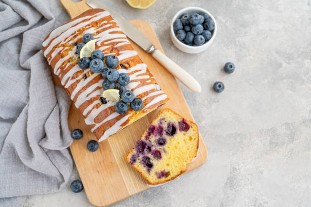 istock Lemon blueberry cake with lemon icing and fresh berries on top on the board on a gray concrete background with cup of tea. Selective focus. Copy space. 1381235856