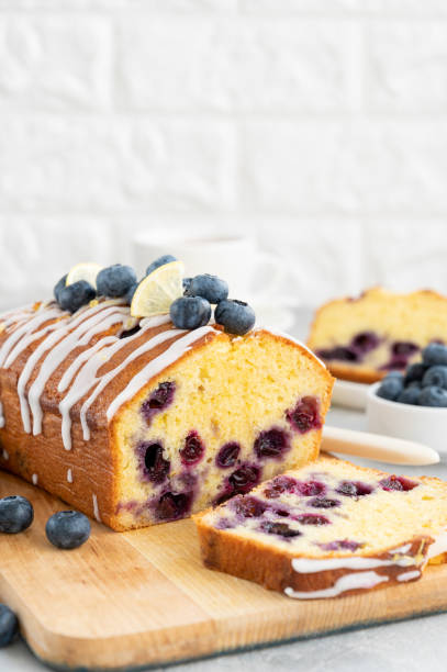 istock Lemon blueberry cake with lemon icing and fresh berries on top on the board on a gray concrete background with cup of tea. Selective focus. Copy space. 1381235862