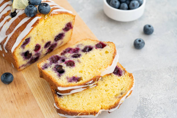 istock Lemon blueberry cake with lemon icing and fresh berries on top on the board on a gray concrete background with cup of tea. Selective focus. Copy space. 1381235868