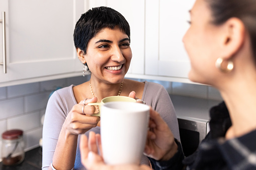 Authentic shot of happy women married homosexual female gay couple having a cup of tea or coffee at home together in the kitchen - lesbian couple at home enjoying life together