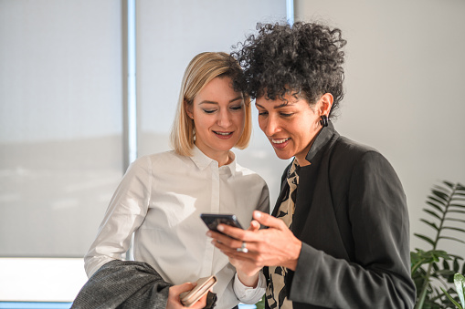 Happy multiracial female business coworkers using smart phone in the office.