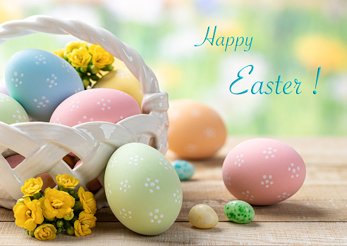 Colored easter eggs with basket and flowers on a wooden table with colorful spring background and Happy Easter text