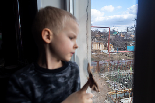 Niño sentado en la ventana y sosteniendo un avión de combate de juguete photo